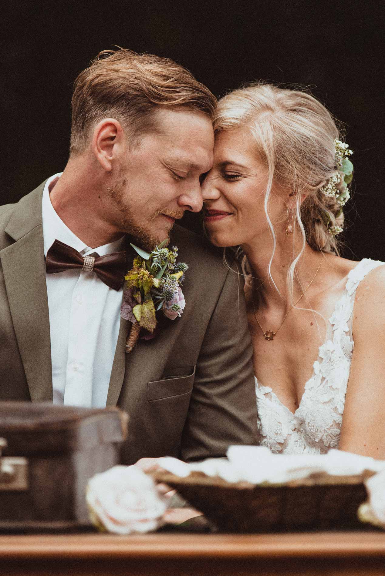 Bride and groom sharing a tender forehead touch, smiling with eyes closed in a deeply emotional moment.